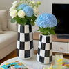 A minimalist black and white checkered ceramic vase holding a bouquet of white and blue hydrangeas.