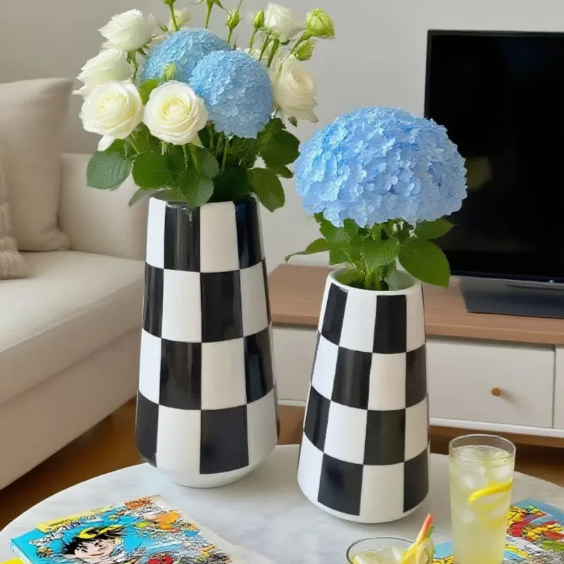 A minimalist black and white checkered ceramic vase holding a bouquet of white and blue hydrangeas.