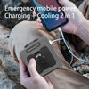 A hand holds a portable waist fan with a built-in flashlight and charging cable in an outdoor setting.