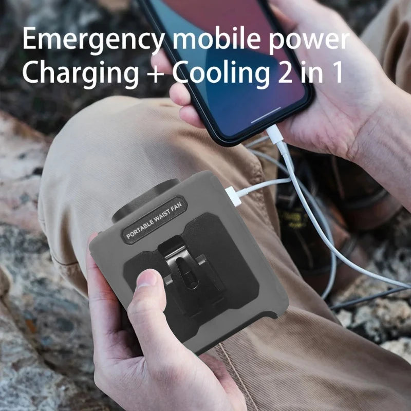 A hand holds a portable waist fan with a built-in flashlight and charging cable in an outdoor setting.