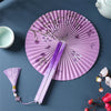 A purple folding fan with a tassel is displayed on a dark blue surface, featuring delicate floral designs.