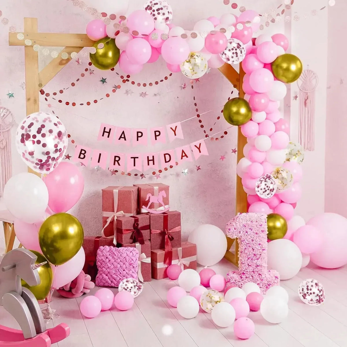 A pink and gold birthday decoration featuring a balloon arch, confetti, and pink and gold balloons.