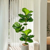 A large artificial ficus tree with green fiddle leaves standing in a white pot indoors.