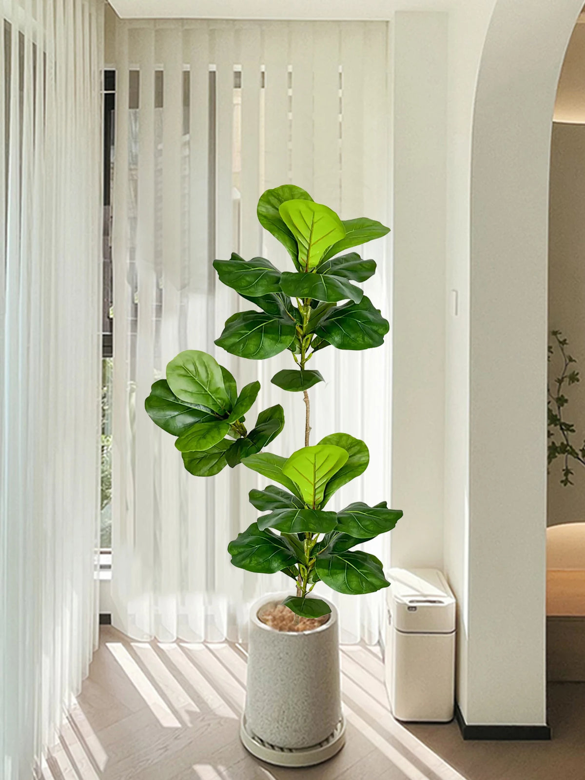 A large artificial ficus tree with green fiddle leaves standing in a white pot indoors.