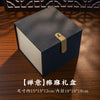 A dark gray box with a brass clasp and a light-colored interior, labeled as a traditional ornament.