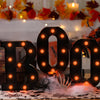 Un letrero de marquesina negro con forma de 'BOO' y luces naranjas brillantes sobre una mesa decorada con hojas de otoño.