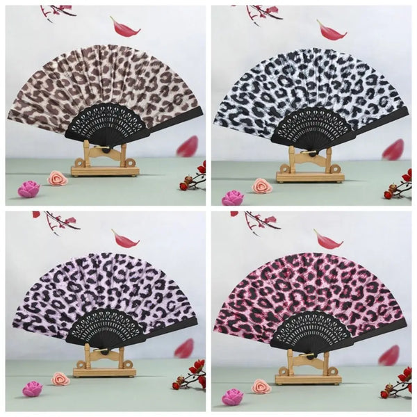 A leopard print folding hand fan with a black handle displayed on a wooden stand.