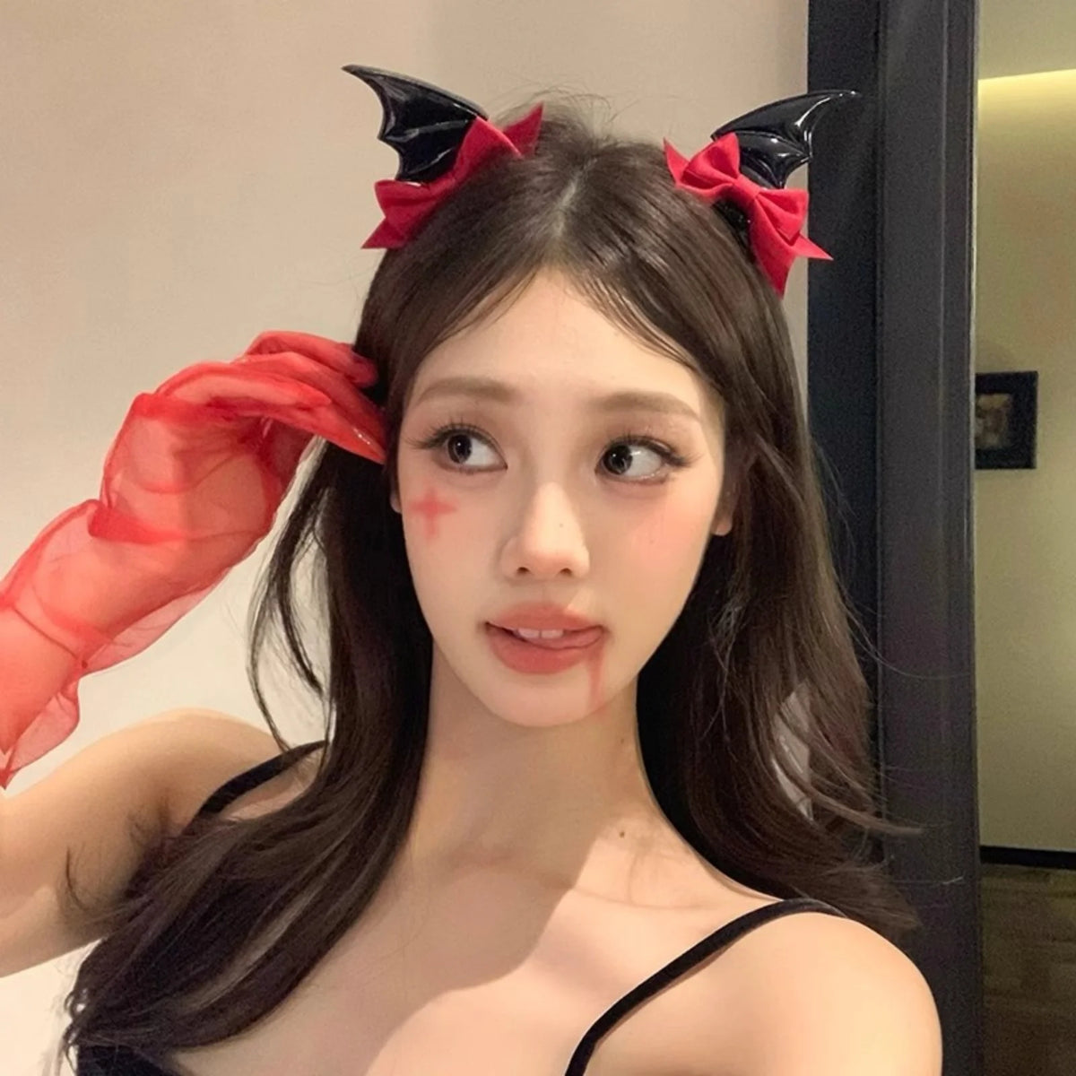 A woman with long dark hair wearing black hair clips shaped like devil horns and bat wings, adorned with red fabric accents.