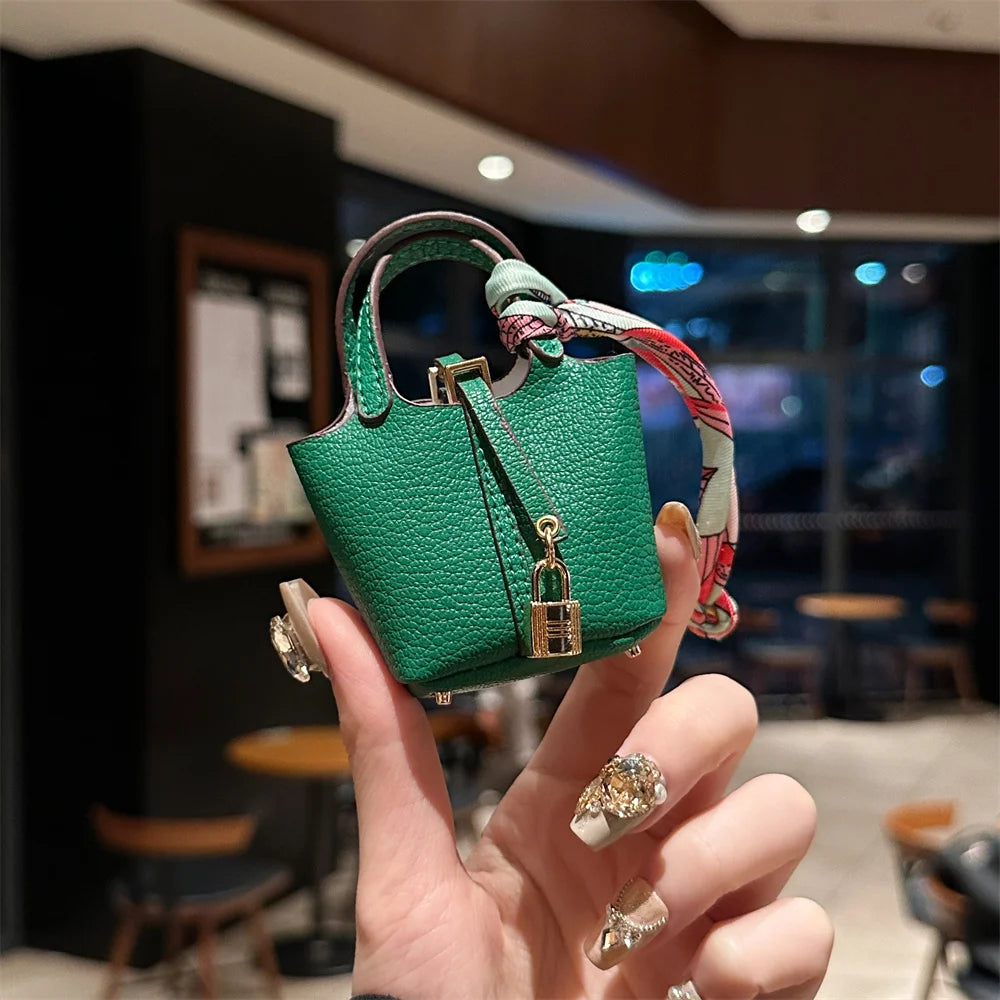 A hand holds a small green mini house handbag with a pink and red wrist strap.