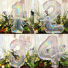 Clear iridescent number balloons spelling out 12, 2, 3, and 4, tied with bows amidst greenery and flowers.