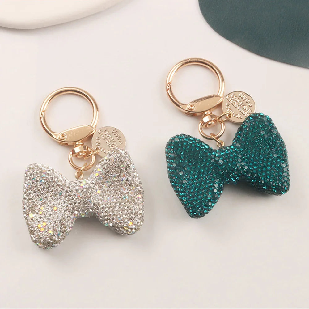 A sparkling silver rhinestone bow keychain with a gold split ring and a teal glitter bow keychain.