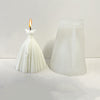A white silicone mold shaped like a wedding dress stands next to a white pillar candle.