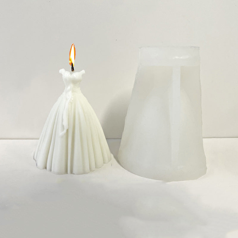 A white silicone mold shaped like a wedding dress stands next to a white pillar candle.