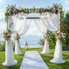 An elegant outdoor wedding backdrop featuring a wooden arch decorated with lush floral arrangements and sheer white tulle dra