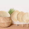A collection of peach-shaped bamboo woven hand fans in natural beige tones displayed on a wooden surface.