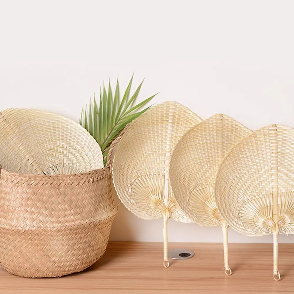 A collection of peach-shaped bamboo woven hand fans in natural beige tones displayed on a wooden surface.