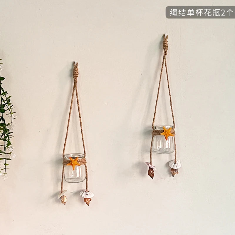 Two hanging decorative glass terrariums with dried flowers and twine on a white wall