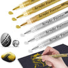 A collection of extra-fine point acrylic paint pens in various colors and finishes shown next to a hand painting on dark pape