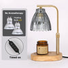 A gold-toned adjustable candle warmer lamp with a glass shade and heating bulbs, sitting on a wooden base.