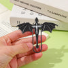 A hand holds a black metal bookmark shaped like a four-winged dragon for reading.