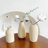 Three minimalist ceramic vases holding dried white cotton stems and greenery on a wooden surface.