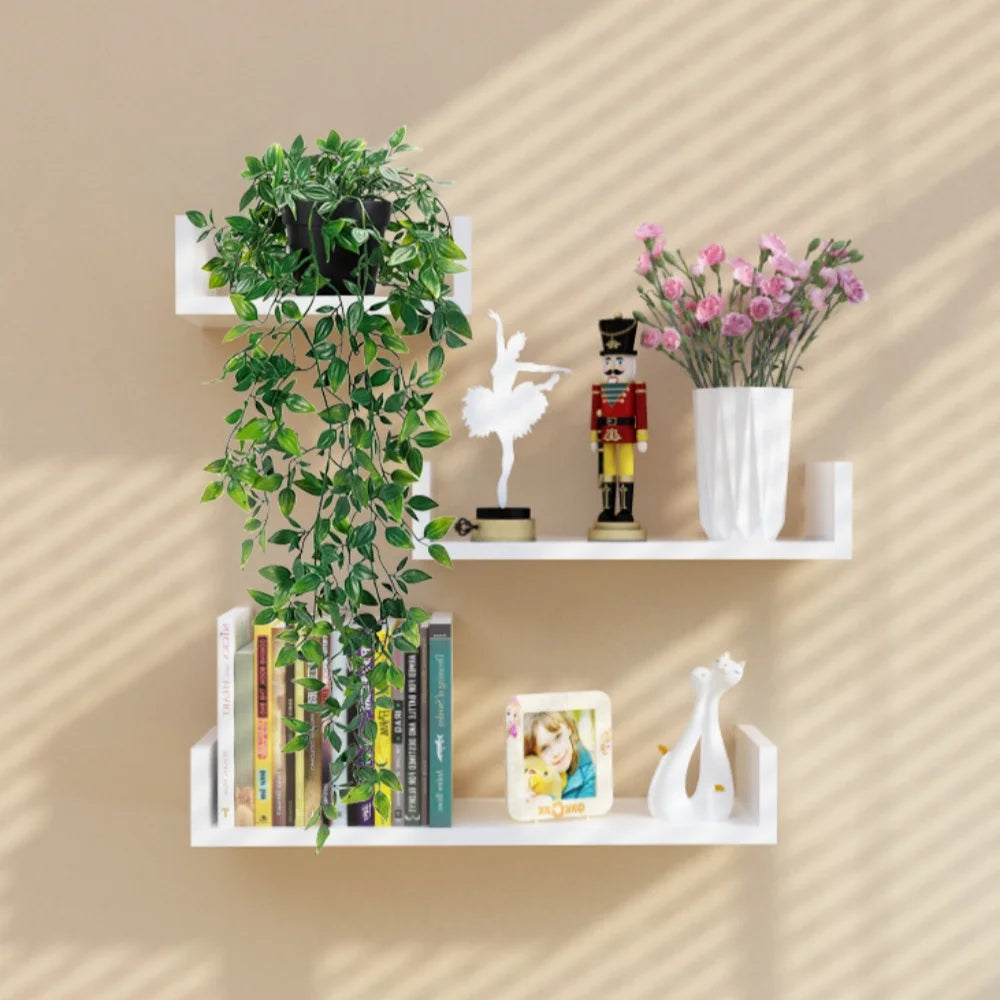 A white shelf display featuring a hanging artificial plant wall decor with green foliage, a white bird figurine, and a vase o