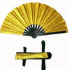 A large, golden, pleated hand fan with a black handle and folding structure.