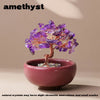 A handcrafted crystal tree with purple amethyst crystals mounted on a copper wire base inside a pink bowl.
