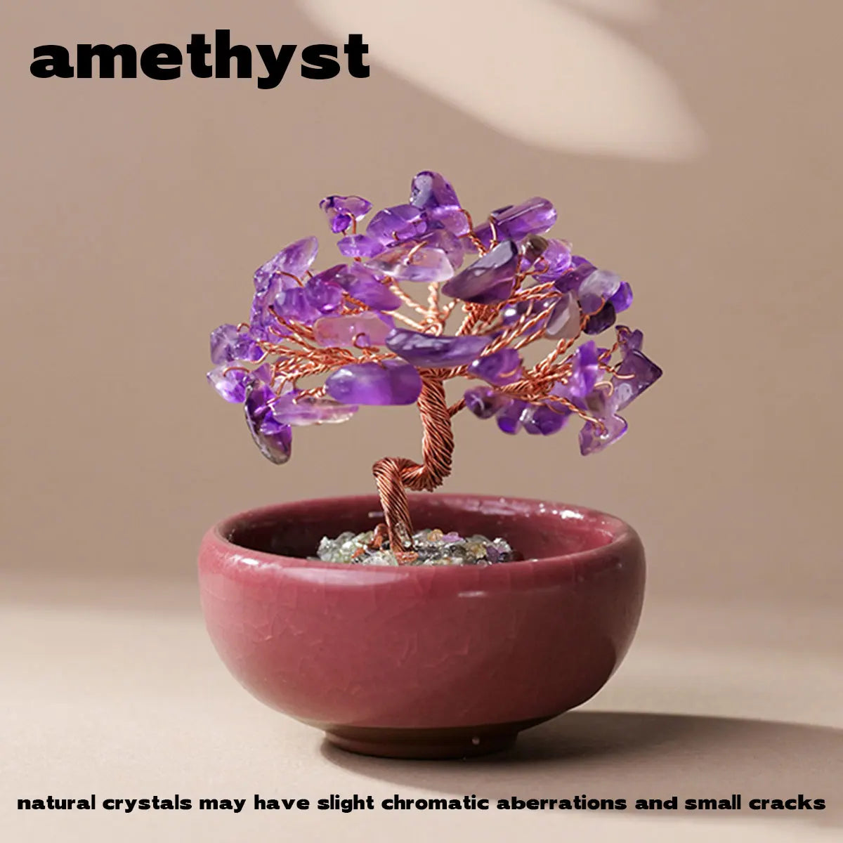 A handcrafted crystal tree with purple amethyst crystals mounted on a copper wire base inside a pink bowl.