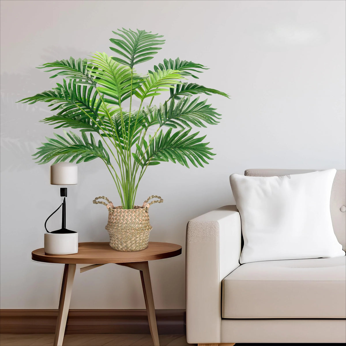 An artificial areca palm tree in a woven pot sits on a wooden table next to a light-colored sofa.