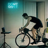 A man is riding a bicycle indoors in front of a neon sign that reads DON'T QUIT.