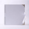 Carnet photo blanc à couverture plate avec coin doré décoratif et ruban blanc noué sur le bord.