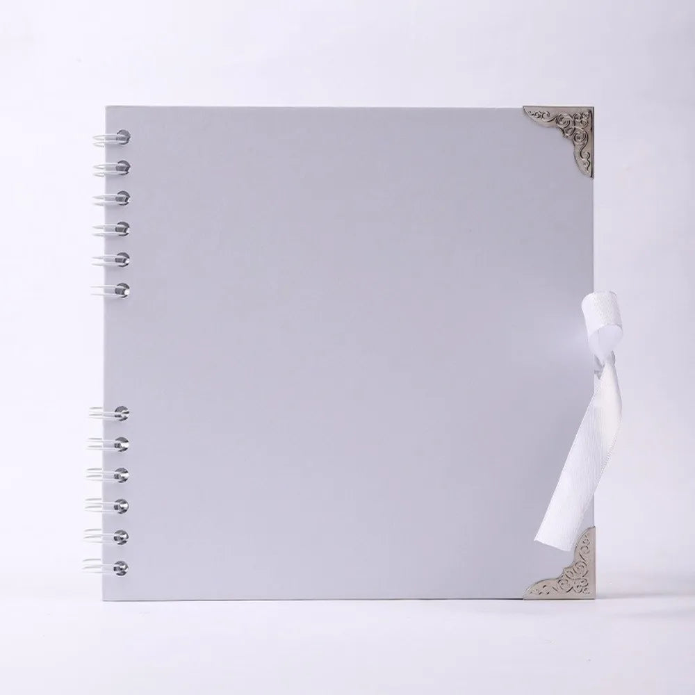 Carnet photo blanc à couverture plate avec coin doré décoratif et ruban blanc noué sur le bord.