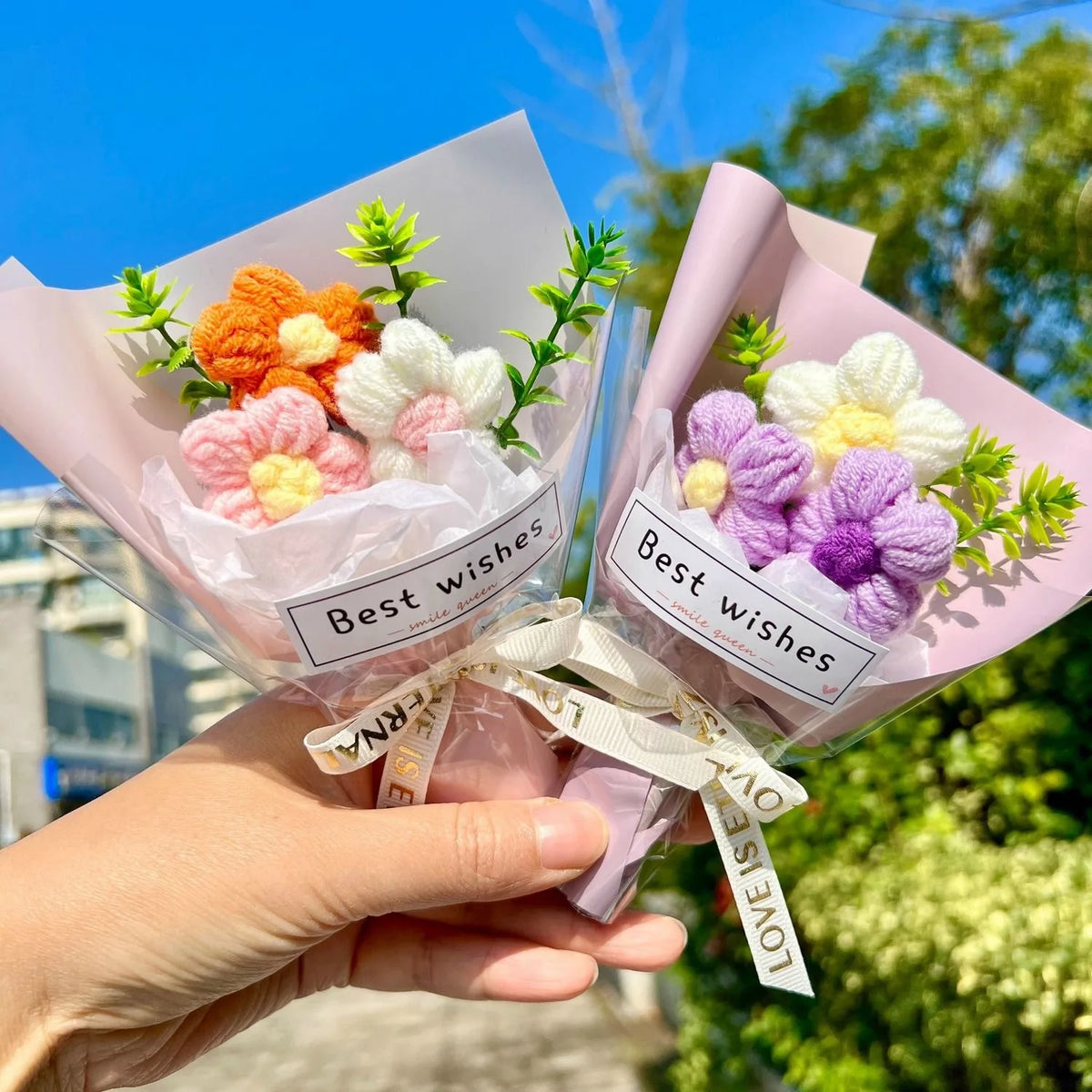 A hand holds a bouquet of handmade crochet sunflower mini flowers in pink paper with a white ribbon.