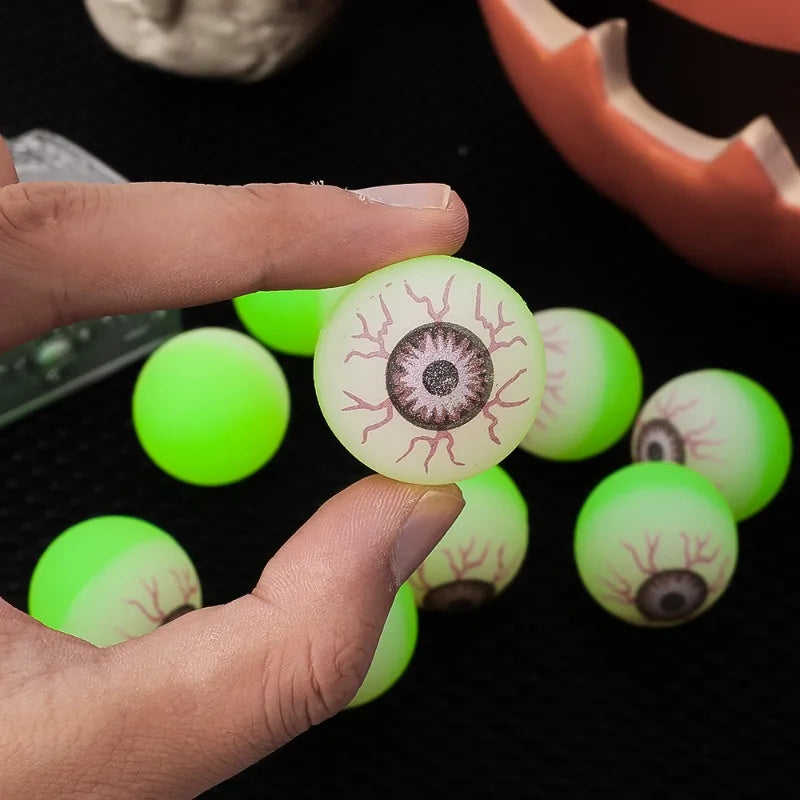 A hand holds several bright green glow-in-the-dark eyeball bouncy balls against a dark background.