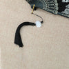 Black bamboo flower antique folding fan with a gold tassel and white pom-pom on a beige fabric background