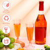 A set of two disposable champagne glasses with a gold finish are shown next to a bottle of orange-colored liquid and fresh gr