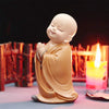 A small, smiling resin figurine of a monk in orange robes sitting in a meditative pose.
