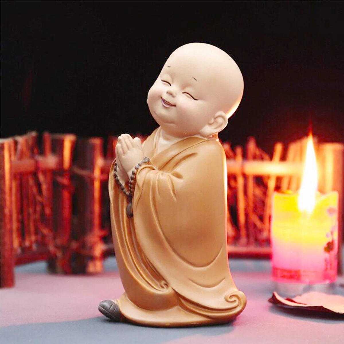 A small, smiling resin figurine of a monk in orange robes sitting in a meditative pose.