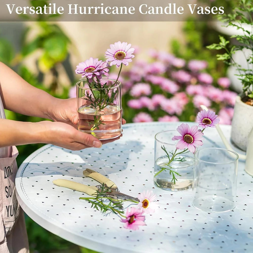 Vases cylindriques en verre transparent élégants remplis de fleurs roses et violettes sur une table blanche.
