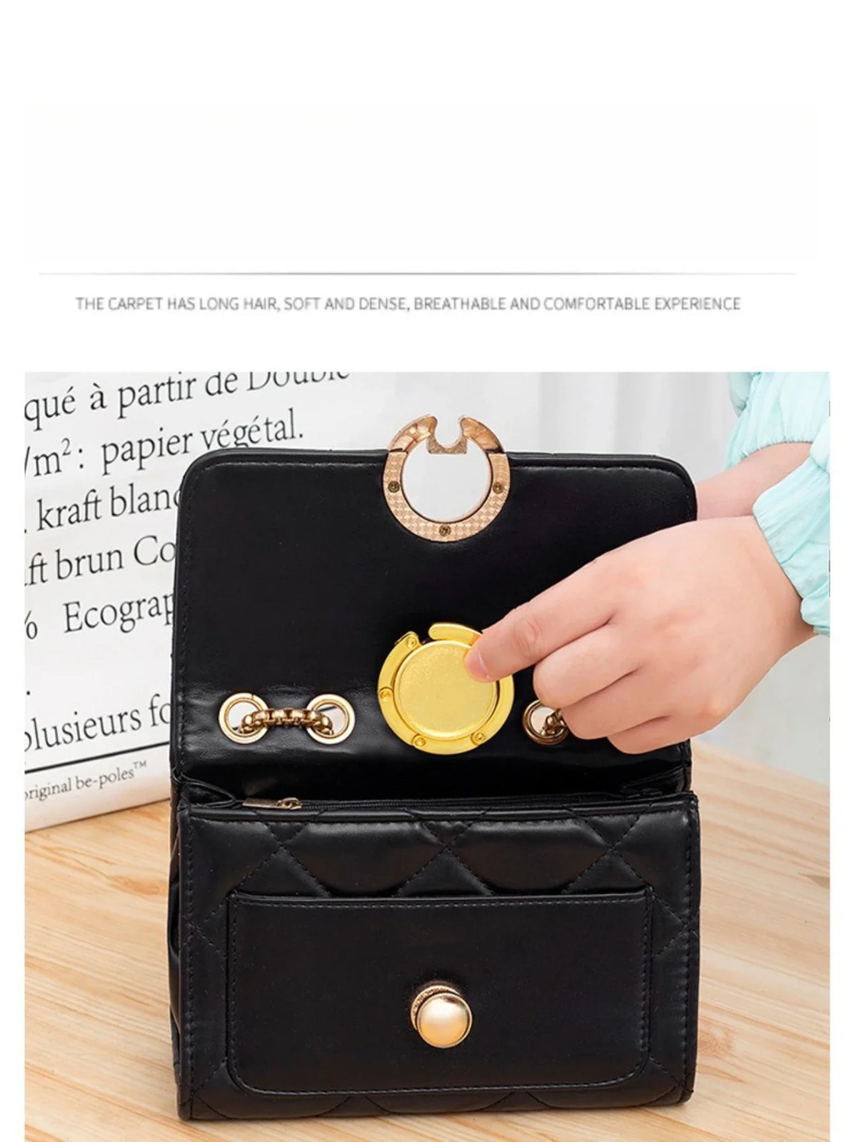 A hand is holding a black compact folding table bag with gold hooks, demonstrating its use as a portable purse hanger.