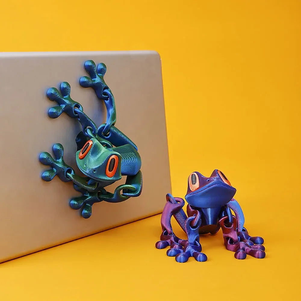 A small, hand-painted 3D printed tree frog ornament with vibrant green and blue colors resting on a yellow surface.