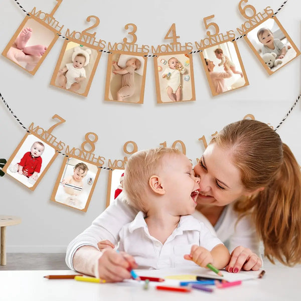 A woman is holding a baby while decorating a banner with monthly growth records for a baby's first birthday.