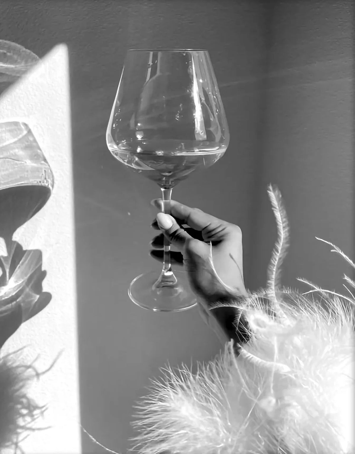 A hand holds a clear wine glass against a bright background, with a black and white art print visible in the foreground.