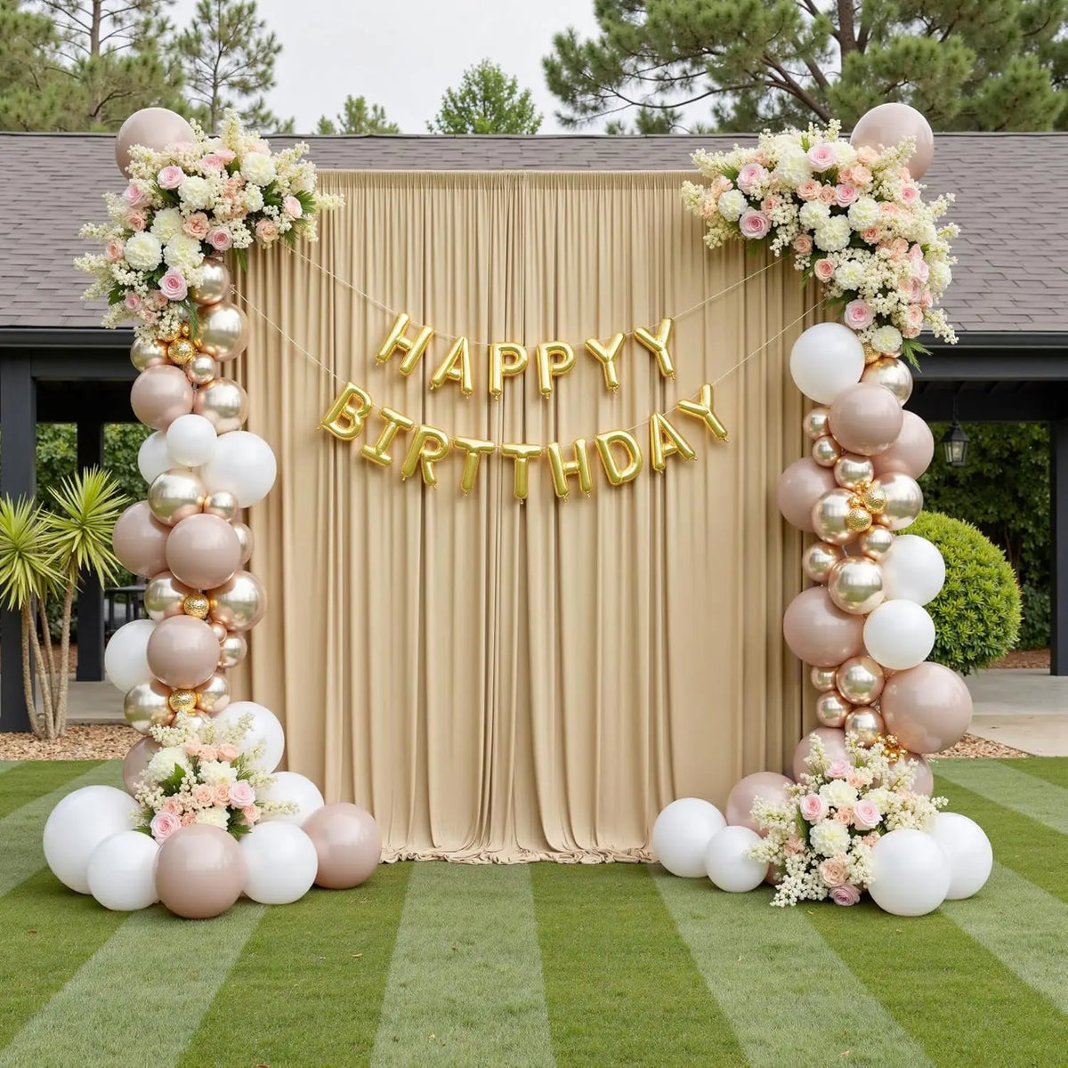 A wedding backdrop featuring a beige curtain with gold lettering and floral arrangements of white and pink roses and greenery