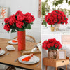 Un vibrante ramo de flores de geranio rojo de seda artificial en una maceta de terracota sobre una mesa de madera.