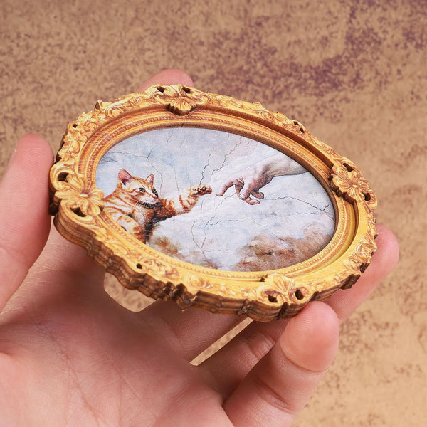 Vintage oval frame with a painting of a cat and hand, used as a fridge magnet.