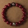 A bracelet made of red cinnabar stones with gold accents, displayed on a brown background.