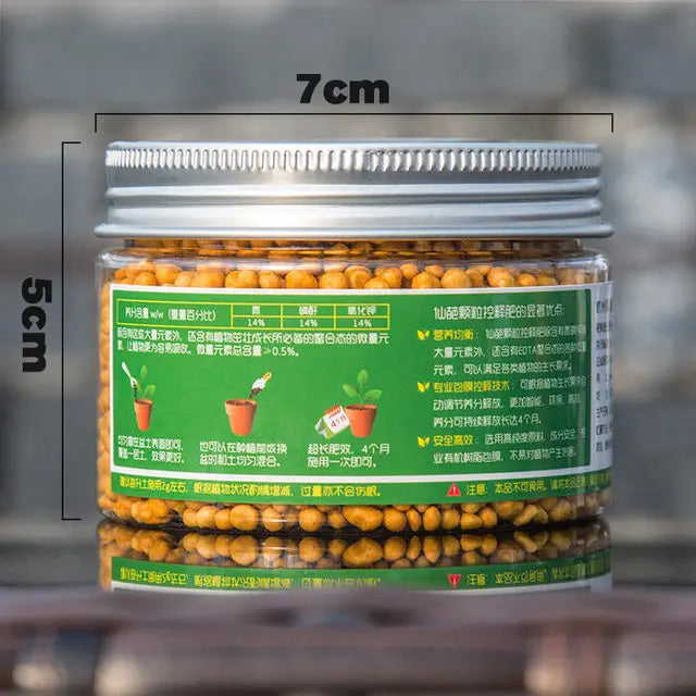 A glass jar of granular slow-release plant fertilizer with a silver lid, showing the product size and instructions.