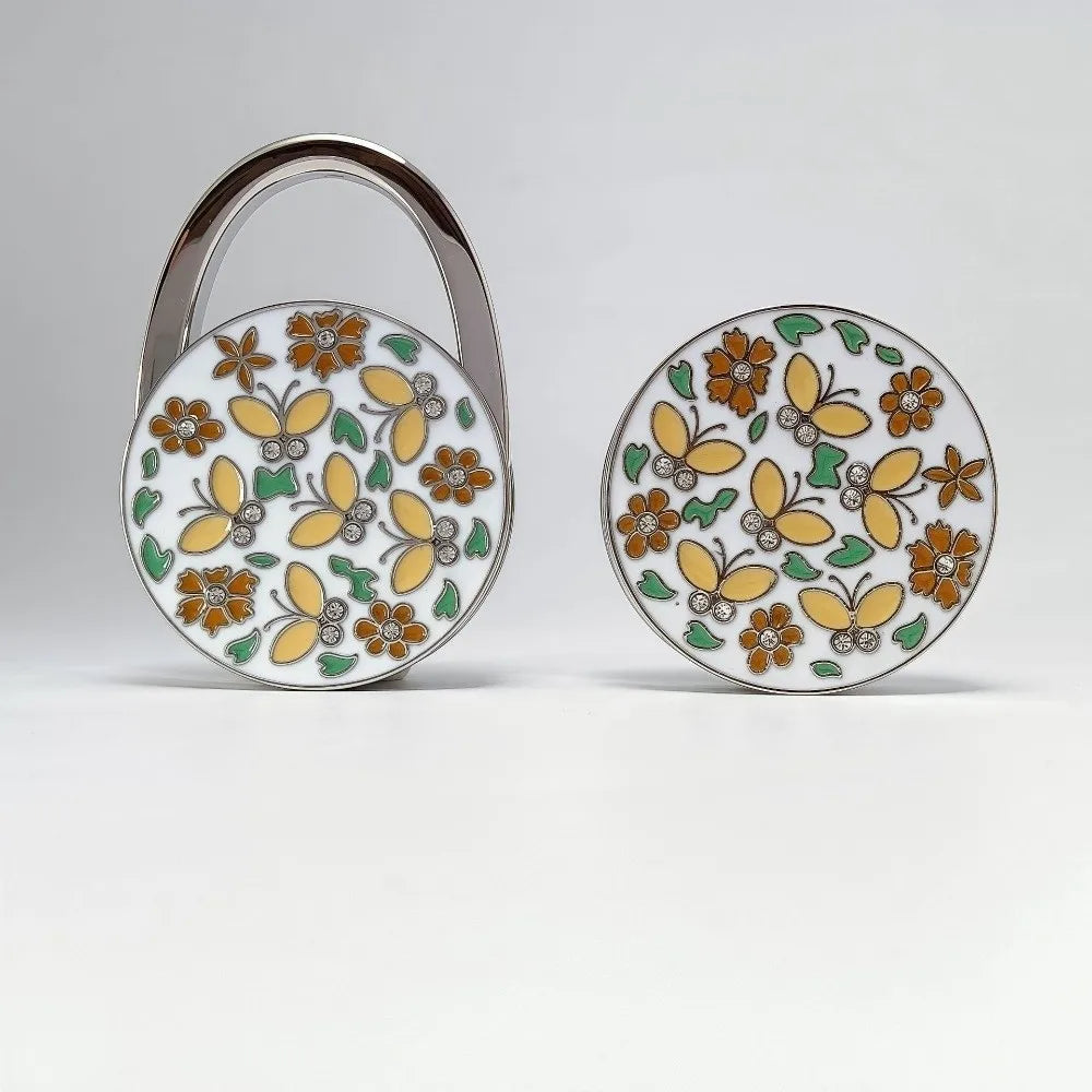 Silver crystal handbag hook with a round floral pattern featuring orange and yellow flowers on a white background